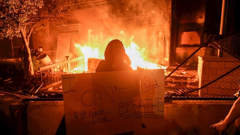Un manifestante sostiene un cartel mientras se quema la comisaria de Minneapolis durante las protestas por el arresto de George Floyd. EFE / CRAIG LASSIG