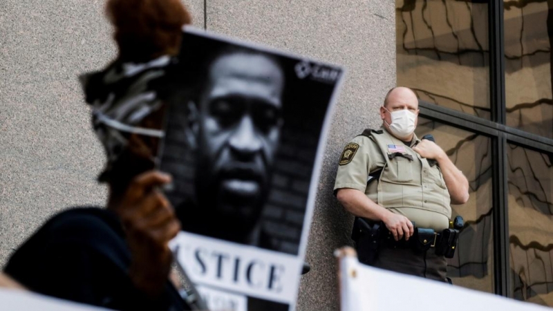 Un oficial de policía con una mascarilla observa a los manifestantes que se reúnen fuera del ayuntamiento en Minneapolis. REUTERS/Carlos Barria