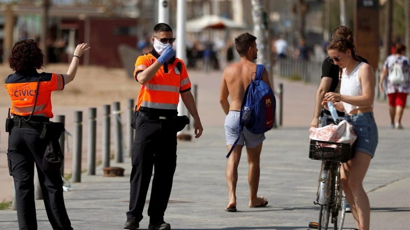 Agentes Civicos indican a una joven que se coloque la mascarilla protectora, este sábado en el paseo marítimo de la Barceloneta en Barcelona. EFE/Toni Albir