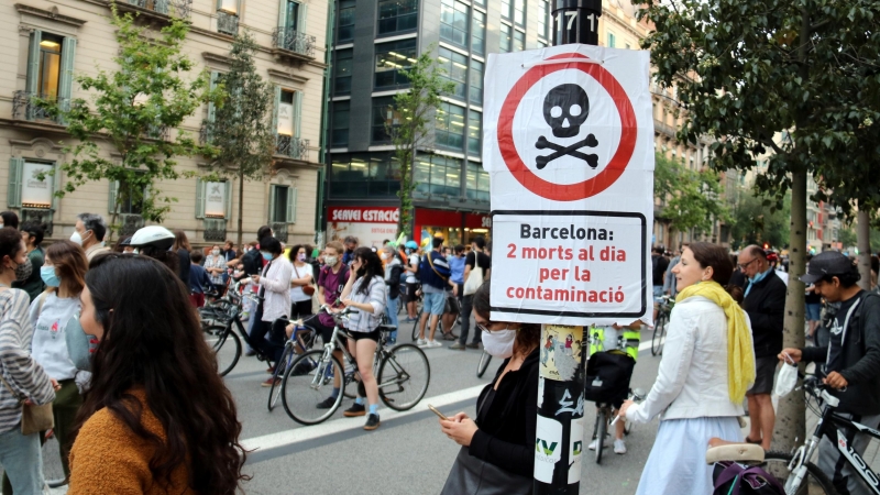 Primer pla d'un cartell que diu que la contaminació mata amb una manifestació contra els cotxes darrere, al centre de Barcelona. ACN / Pol Solà