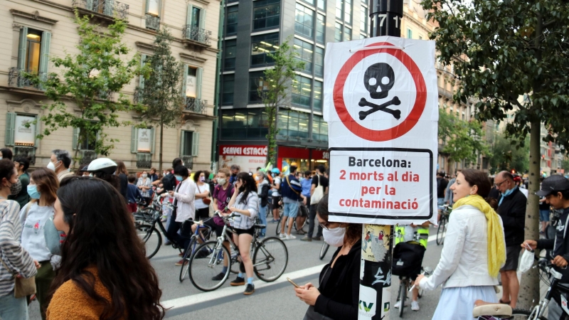 Primer pla d'un cartell que diu que la contaminació mata amb una manifestació contra els cotxes darrere, al centre de Barcelona. ACN / Pol Solà
