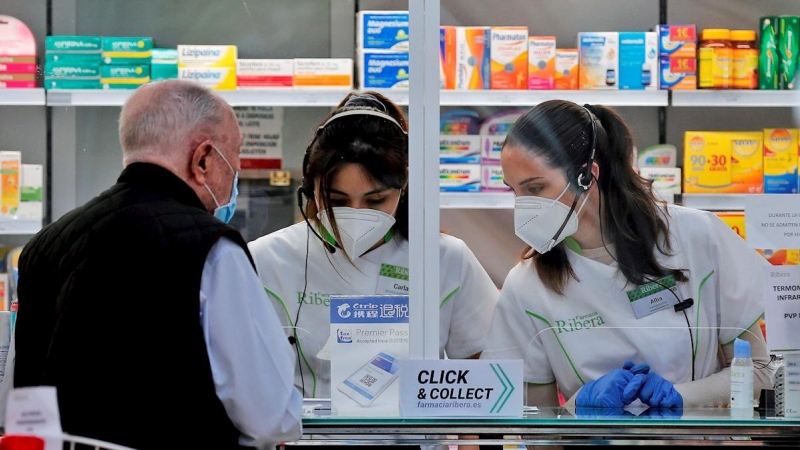 Dos empleadas de una farmacia atienden a un cliente, en una imagen de archivo. / EFE- MANUEL BRUQUE