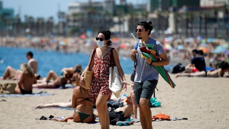 BARCELONA, 24/06/2020.- Dos personas llegan a la playa de la Barceloneta, tras la noche en la que se ha vivido una verbena de San Juan atípica por la pandemia de la COVID-19, en la que las playas de la ciudad han permanecido cerradas para evitar aglomerac