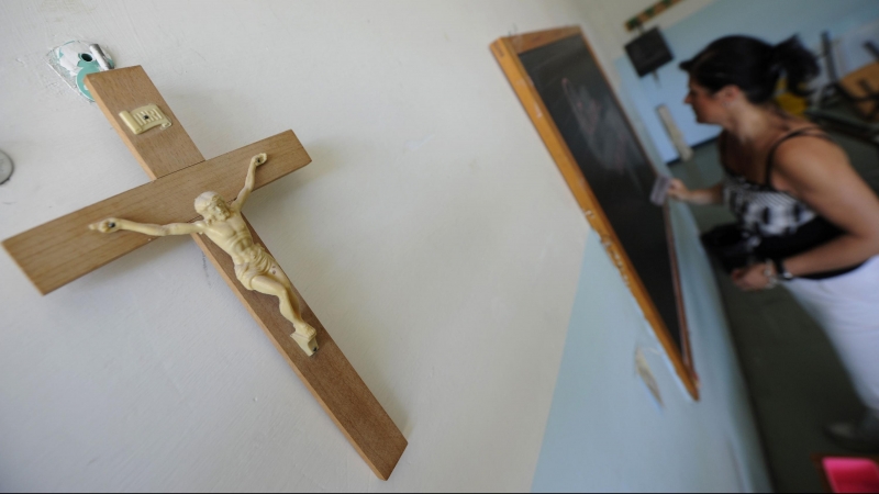 Un crucifijo cuelga en la pared de un aula en el que una profesora escribe en la pizarra. AFP