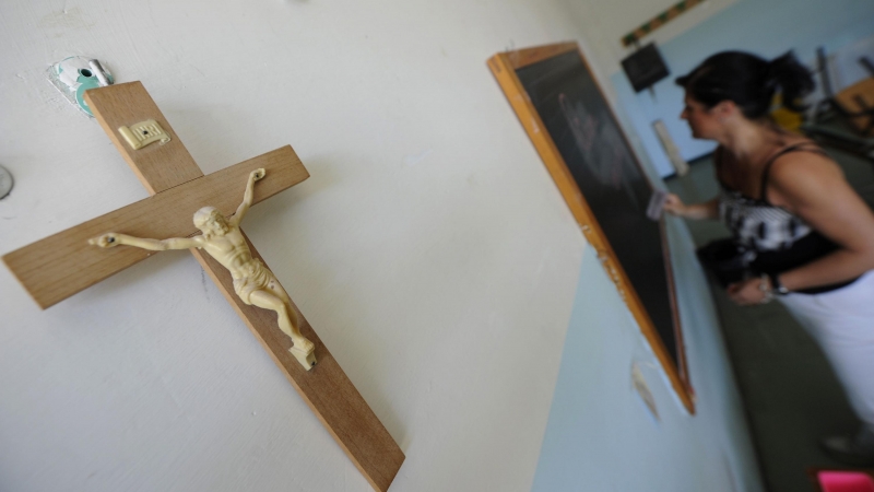 Un crucifijo cuelga en la pared de un aula en el que una profesora escribe en la pizarra. AFP