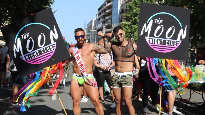 Dos participants de la desfilada del Pride BCN 2018 mostrant el cartell del club The Moon Night Club i amb roba de la marca Addicted. Júlia Pérez | ACN