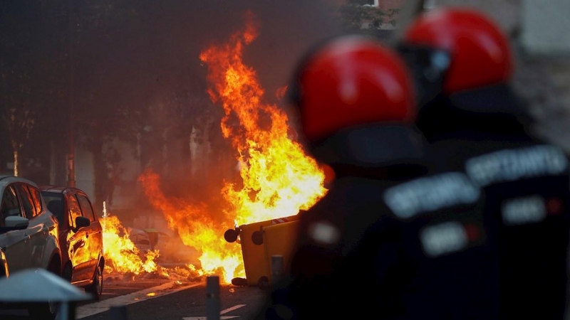 , 03/07/2020.- Agentes de la Ertzaintza observan un contenedor ardiendo en las calles de San Sebastián, donde la formación política Vox celebra esta tarde un acto electoral. EFE/Juan Herrero