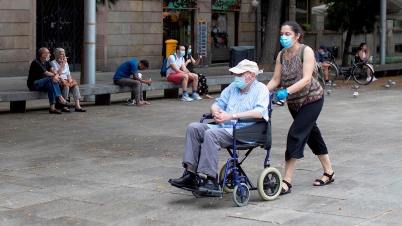Una mujer empuja la silla de un anciano en el centro de Barcelona.  - EFE