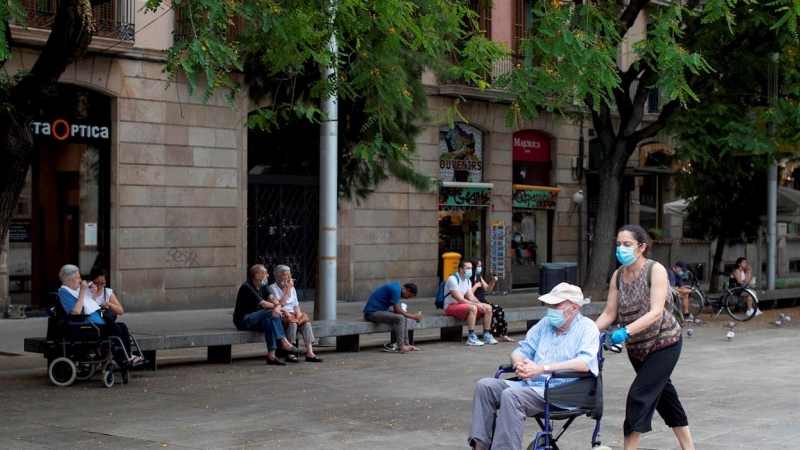 Una mujer empuja la silla de un anciano en el centro de Barcelona.  - EFE