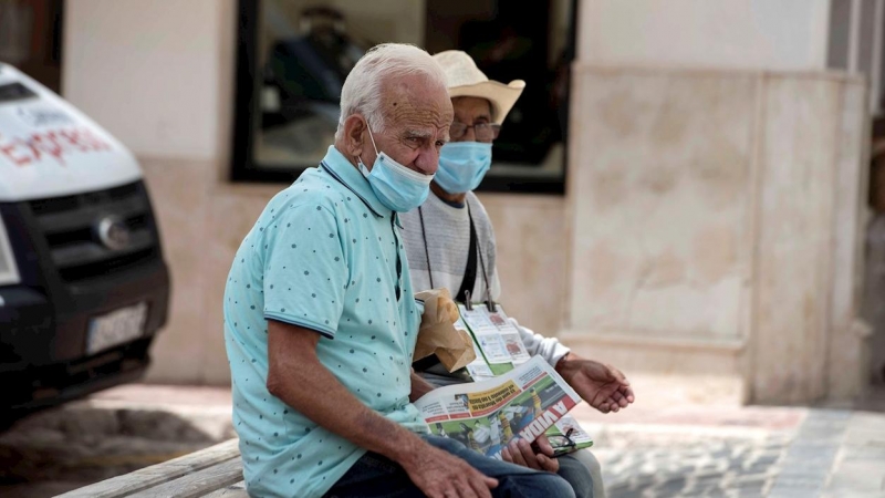 Una pareja de ancianos se protegen con mascarillas mientras descansan en un banco en Mahón, este jueves. | EFE