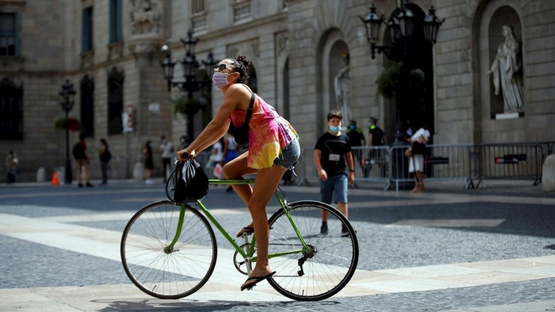 Una joven pasea con su bicleta , protegida con su mascarilla, este jueves, primer día en que es obligatorio el uso de mascarillas en toda Cataluña aunque se puedan guardar las distancias.EFE/Toni Albir