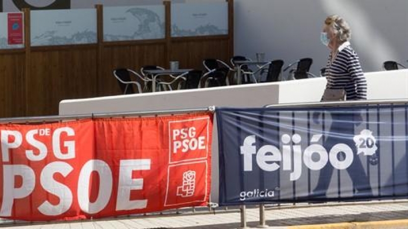 Una mujer protegida con mascarilla pasea junto a carteles electorales del PPdeG y del PSdeG en Foz, en la comarca de A Mariña, Lugo, (Galicia). / Europa Press