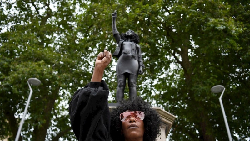 La manifestante Jen Reid con el puño en alto posa frente a una representación de sí misma, la estatua 'A Surge of Power (Jen Reid)' del artista británico Marc Quinn. EFE / EPA / NEIL HALL