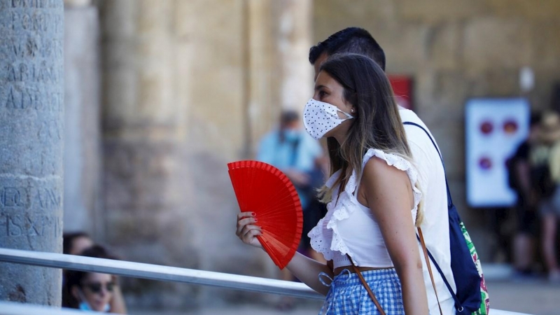 Una mujer protegida con unas mascarilla mientras se abanica para aliviar las altas temperaturas de este jueves en Córdoba. | EFE