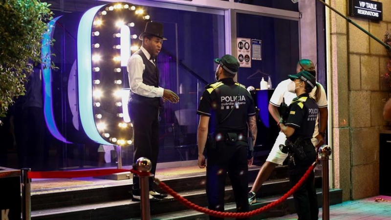 Una patrulla de la Guardia Urbana de Barcelona conversa con un trabajador de un local de ocio nocturno, anoche, que cerró a medianoche para cumplir con el mandato decretado por las autoridades catalanas para evitar la propagación del coronavirus. EFE/Quiq