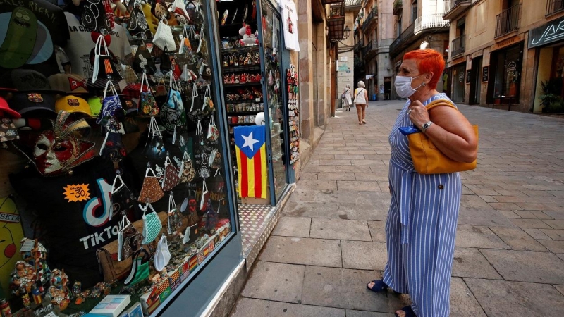 Una mujer con mascarilla, delante de una tienda de souvenirs turísticos en Barcelona. REUTERS