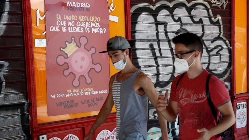 MADRID, 04/08/2020.- Dos jóvenes pasan ante un cartel alusivo al coronavirus en el centro de Madrid, este martes 4 de agosto, EFE/Mariscal