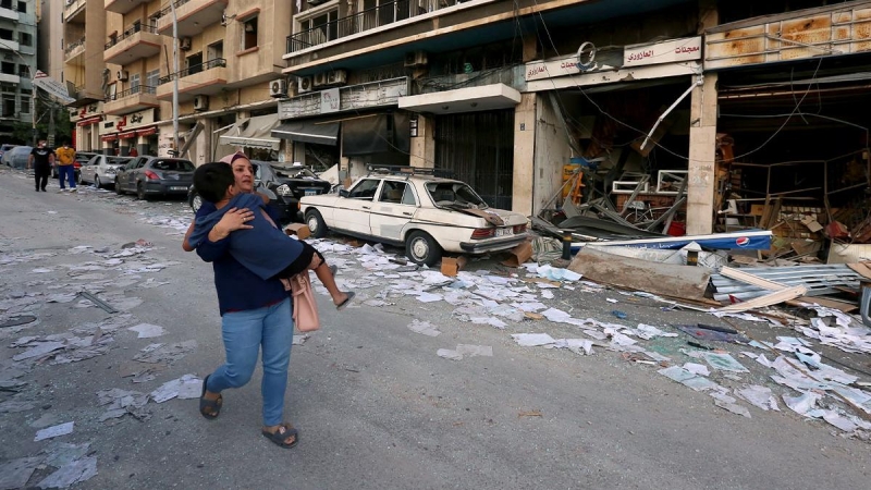 Una mujer lleva a un niño mientras pasa por las tiendas dañadas tras la explosión del martes en Beirut, Líbano