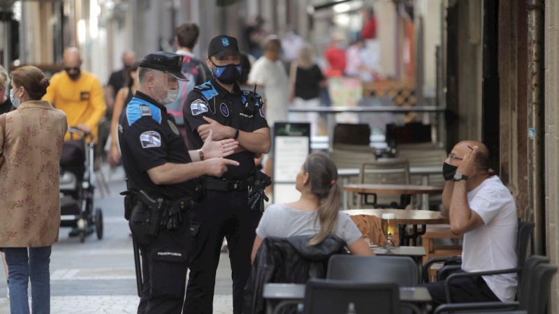 Dos agentes de la Policía local de A Coruña se dirigen a un hombre que se encontraba fumando en una terraza de un bar de la ciudad. EFE/ CABALAR