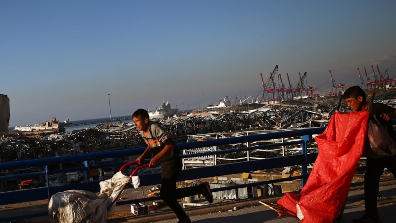 Jóvenes corriendo frente a los escombros de la explosión en el puerto de Beirut. / REUTERS