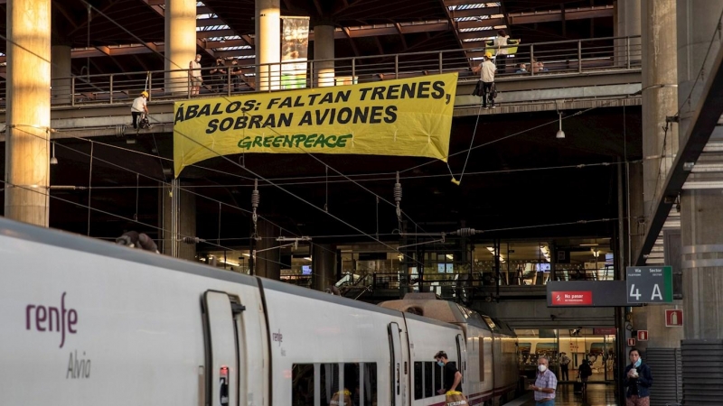 Activistas de Greenpeace han desplegado esta mañana una pancarta sobre las vías de Atocha para denunciar la falta de trenes en un verano marcado por la crisis de la covid-19. Bajo el texto 'Ábalos: faltan trenes, sobran aviones'. EFE/Pablo Blázquez