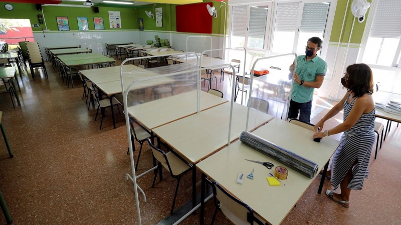 Xavi Leal y Carolina Ramos, director y jefa de estudios, respectivamente, del CEIP Jaume I de Catarroja, colocan los parabanes, realizados con unos percheros y una lámina de plástico transparente, para prepararse para la vuelta a las aulas en la Comunita