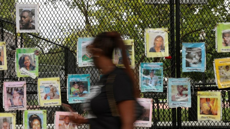 Una mujer pasa por delante de fotografías de personas asesinadas por la Policía, colgadas en una valla de seguridad cerca de la Casa Blanca. REUTERS / Jonathan Ernst