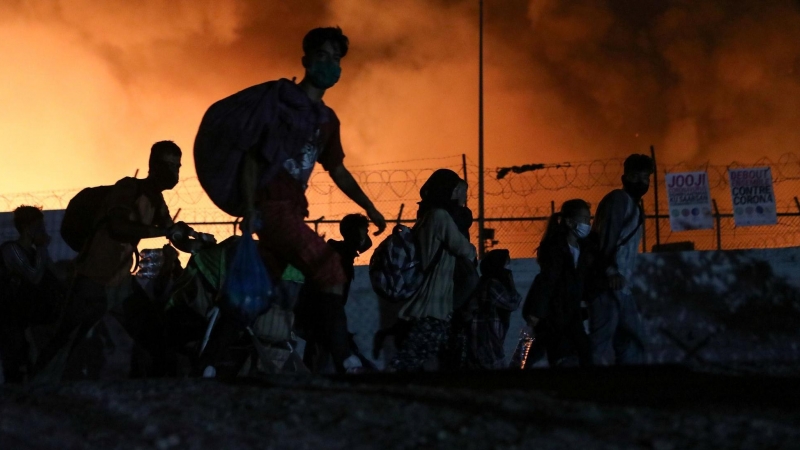 Un grupo de refugiados carga con sus pertencias mientras huye del incendio que ha arrasado el masificado campo de Moria, en Lesbos, Grecia, días después de que se detectara el primer positivo por covid.- REUTERS.