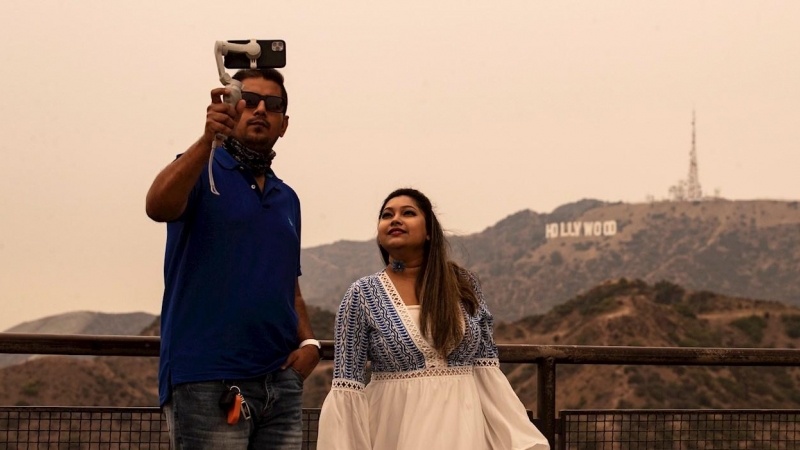 Venice (United States), 11/09/2020.- A duo take a selfie within view of the Hollywood sign under an orange overcast sky in the afternoon in Los Angeles, California, USA, 10 September 2020. California wildfire smoke high in the atmosphere all over the stat