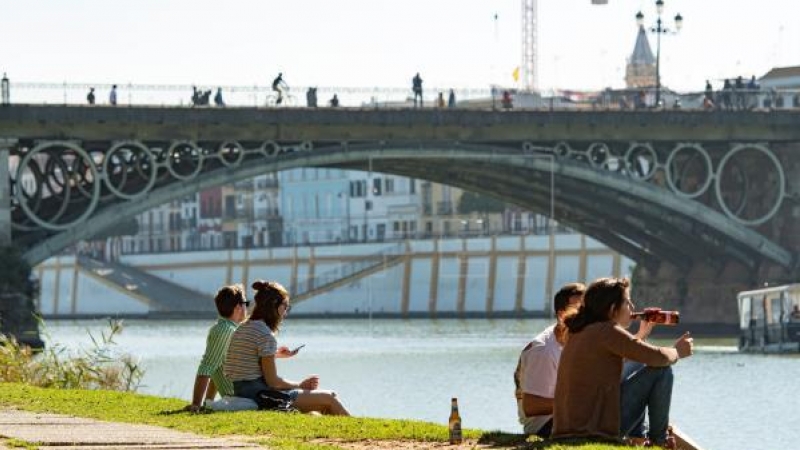 Varias personas se relajan en la orilla del Guadalquivir junto al Puente de Triana de Sevilla / EFE