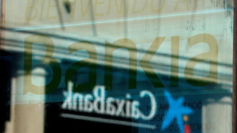 El logo de una oficina de Caixabank se refleja en el ventanal de una sucursal de Bankia en Barcelona. REUTERS