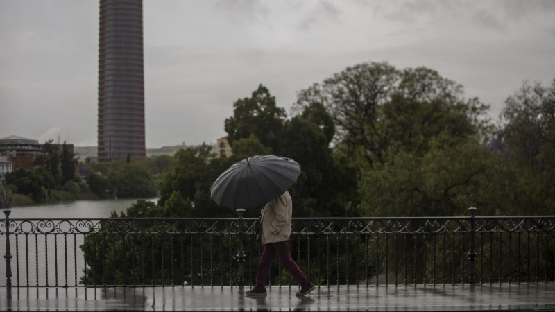Un hombre protegido con un paraguas camina por el puente de Triana durante la alerta amarilla por tormentas en Sevilla. María José López / Europa Press / Archivo