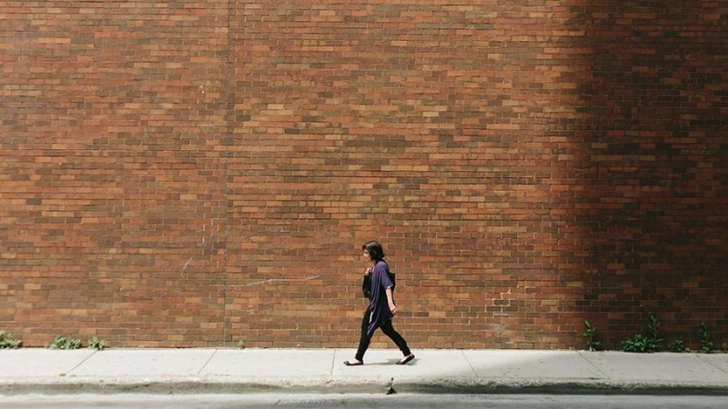 Una mujer camina junto a un muro de ladrillo.- Greg Shield / Unsplash