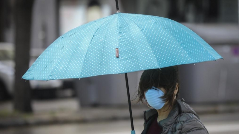 Una mujer protegida con mascarilla y guantes se resguarda de la lluvia bajo su paraguas. María José López / Europa Press / Archivo