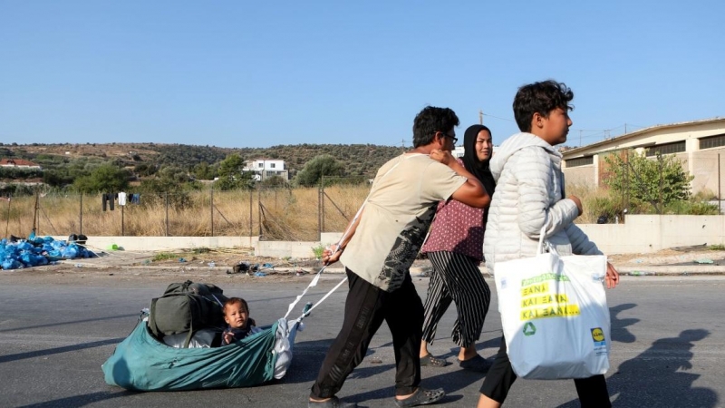 Un hombre tira de un bebé mientras los refugiados y migrantes de la destruida Moria se dirigen hacia un nuevo campamento temporal durante una operación policial, en la isla de Lesbos. REUTERS / Elias Marcou