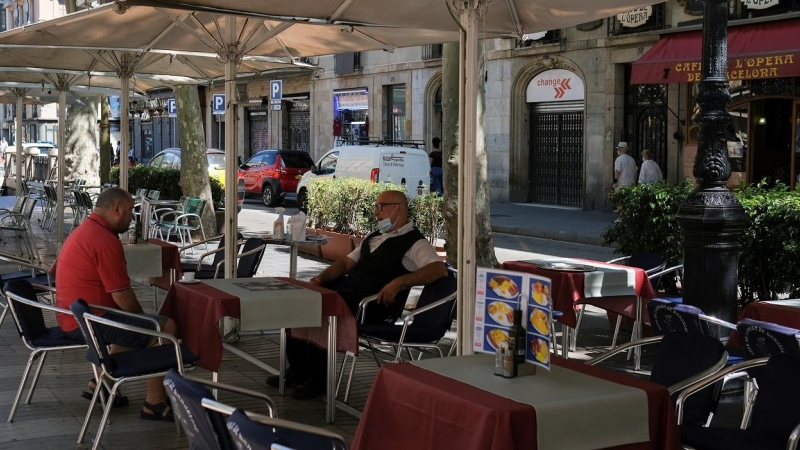 Un camarero, con mascarilla, espera sentado en una mesa la llegada de clientes a la terraza de un bar en las Ramblas de Barcelona. REUTERS/Nacho Doce