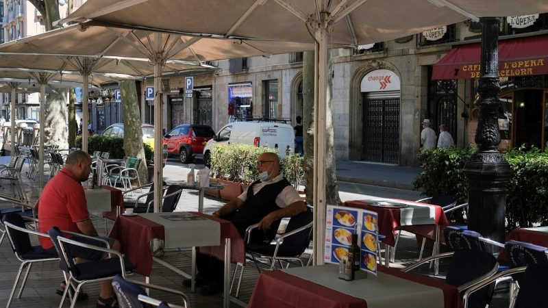 Un camarero, con mascarilla, espera sentado en una mesa la llegada de clientes a la terraza de un bar en las Ramblas de Barcelona. REUTERS/Nacho Doce