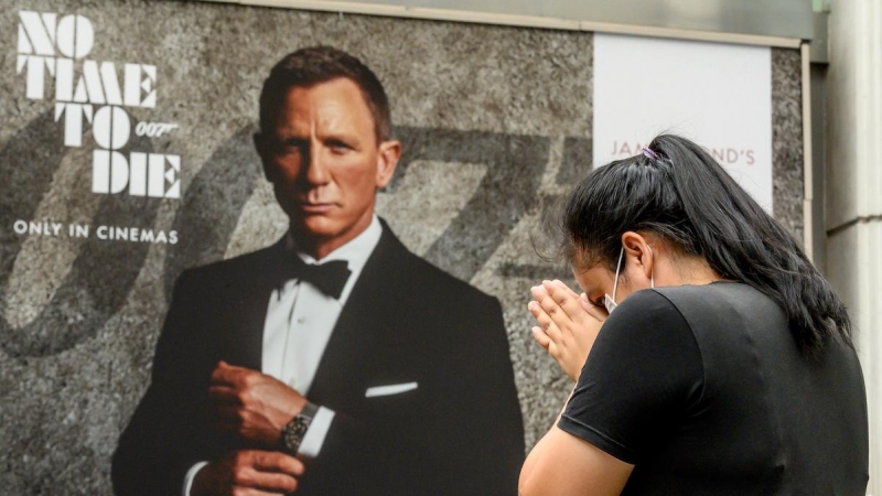 Una mujer reza frente a un cartel publicitario que presenta a Daniel Craig en la nueva película de James Bond.- AFP