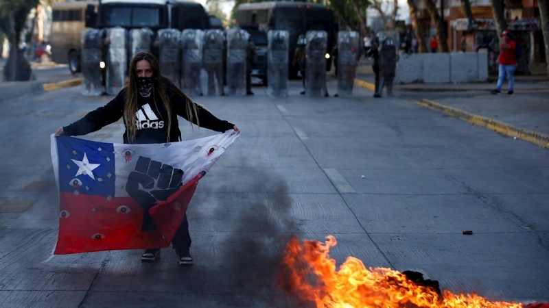 Una manifestante sostiene un a bandera de Chile frente a un contingente de Fuerzas Especiales de Carabineros durante una protesta en la Plaza Italia de Santiago. EFE/Alberto Valdés