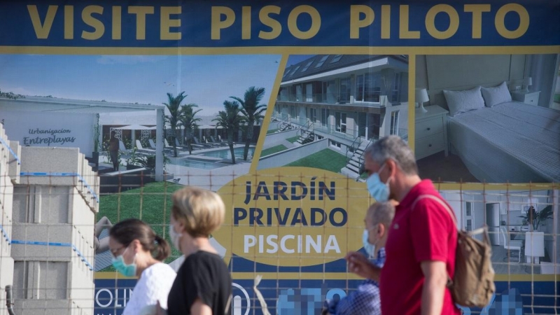 Varias personas caminan junto a un cartel de viviendas en venta en A Mariña (Lugo/Galicia). Carlos Castro / Europa Press / Archivo