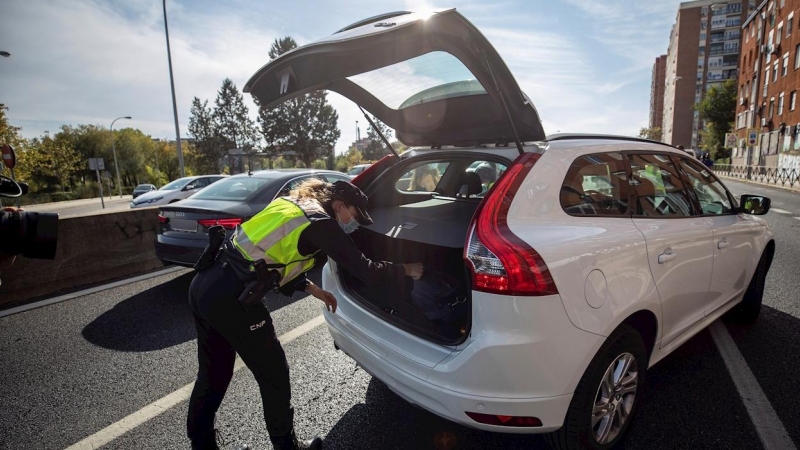 Una agente de la Policía Nacional registra el maletero de un coche durante uno de los controles en las salidas de Madrid. - EFE