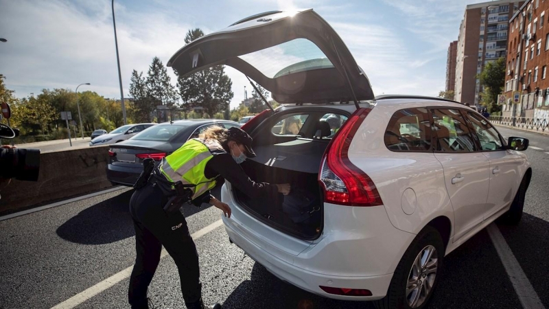 Una agente de la Policía Nacional registra el maletero de un coche durante uno de los controles en las salidas de Madrid. - EFE