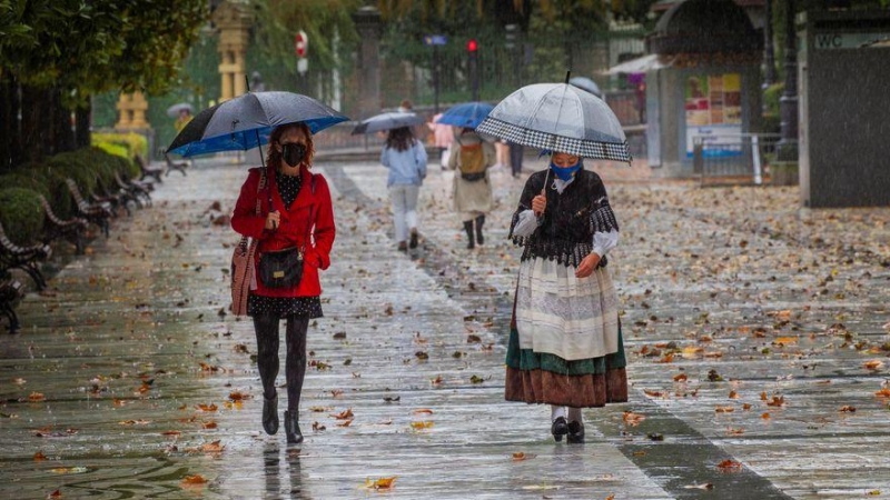 Dos mujeres pasean bajo la lluvia en el paseo de Los Álamos, en el centro de Oviedo, Asturias. EFE/Alberto Morante