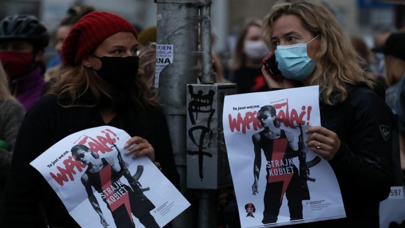 Dos mujeres sostienen pancartas con el lema 'Huelga de mujeres' mientras los manifestantes bloquean una calle durante una protesta contra el fallo del Tribunal Constitucional de Polonia.