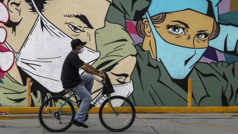 Un hombre pasa en bicicleta frente a un mural en Ciudad Juárez.