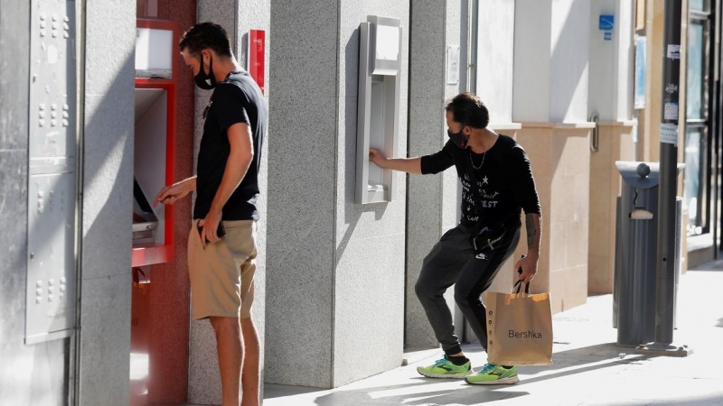 Dos jóvenes operan en sendos cajeros automáticos de dos entidades bancarias, en la localidad malagueña de Ronda. REUTERS/Jon Nazca