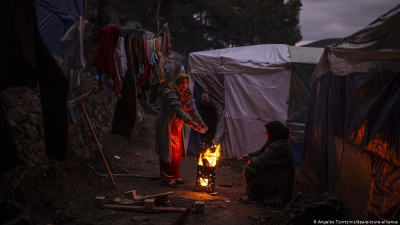 Una refugiada se calienta en un fuego en el campo de acogida de Samos.