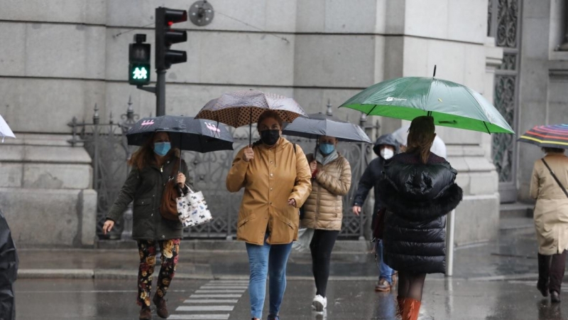 Transeúntes caminan por el centro de la capital protegiéndose de la lluvia con paraguas, en Madrid.