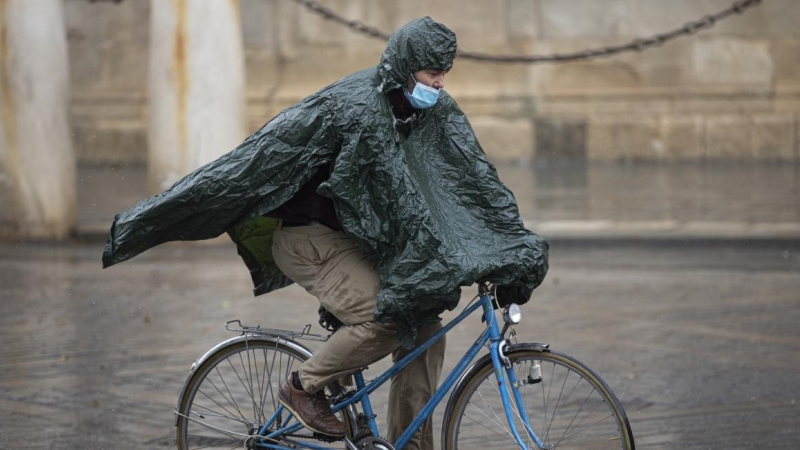 Un hombre circula en bicicleta protegido de la lluvia con un impermeable.