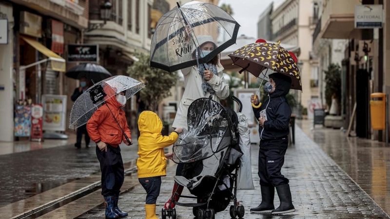 Una mujer con tres menores se protegen de la lluvia con paraguas y chubasqueros en una céntrica calle de València.